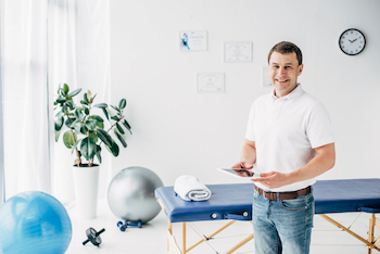 smiling chiropractor holding Digital Tablet in hospital and looking at camera